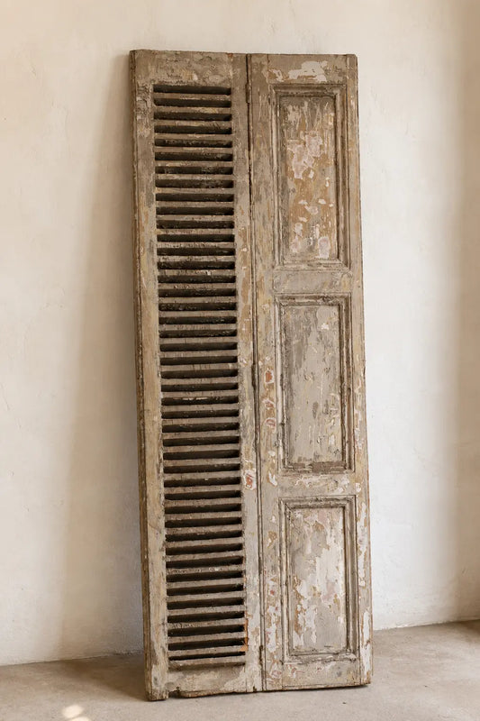 Postigo con celosía vintage apoyado en muro, con pintura envejecida y paneles de madera
